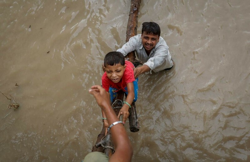  A man helps his son to climb onto a flyover under construction, after being displaced by the rising water level of river Yamuna after heavy monsoon rains in New Delhi, India, July 12, 2023. Photo via Reuters. 