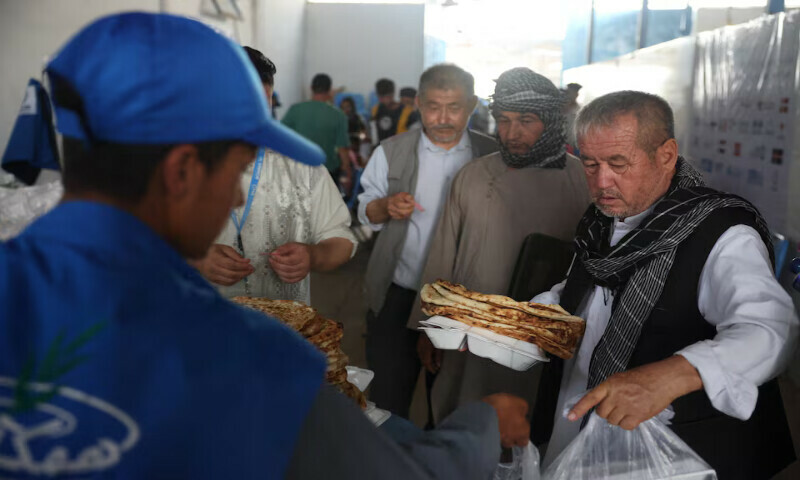 Afghan nationals receive food inside a UNHCR tent at a camp for returning migrants near the Islam Qala border crossing in Herat province, Afghanistan. – Reuters