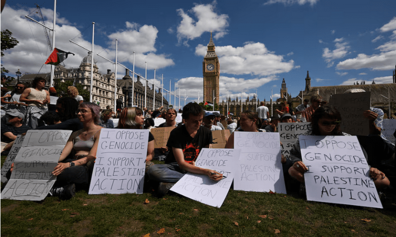 People holding signs sit during a rally organised by Defend Our Juries, challenging the British government’s proscription of “Palestine Action” under anti-terrorism laws, in Parliament Square, in London, on August 9, 2025. Reuters