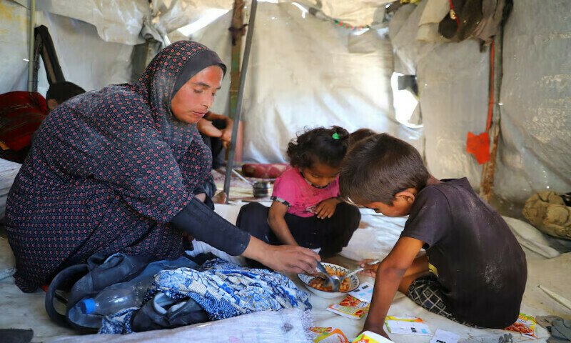 Displaced Palestinian mother Zainab Dakka eats canned beans with her children inside their tent in Gaza City. – Reuters file