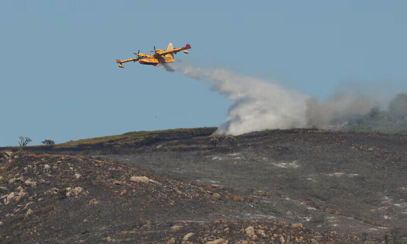 An aircraft drops water over an area burned by a wildfire in the Atlanterra area in Tarifa, Spain. – Reuters