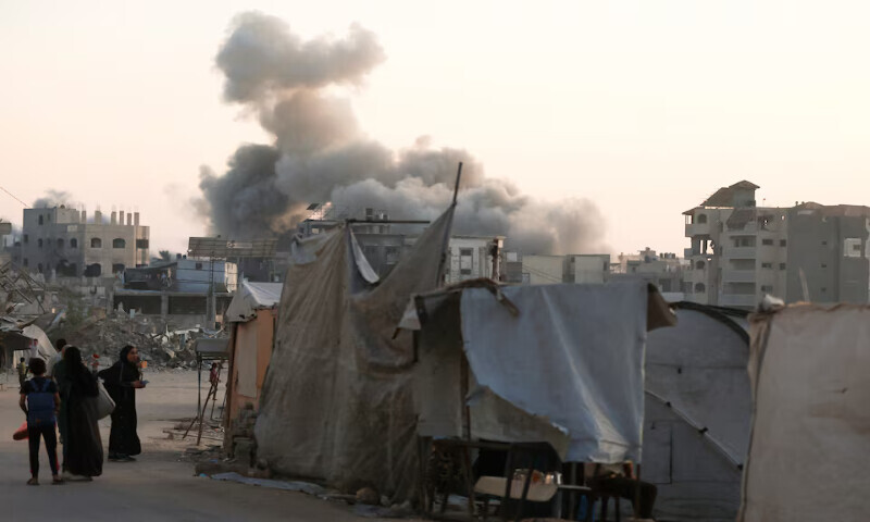 Palestinians stand as smoke rises following an Israeli strike in Gaza City. – Reuters