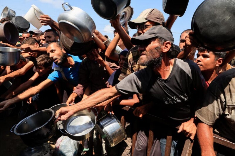 Palestinians reach out with pots and containers while waiting to receive food from a charity kitchen in Khan Younis, southern Gaza Strip, August 21, 2025. REUTERS