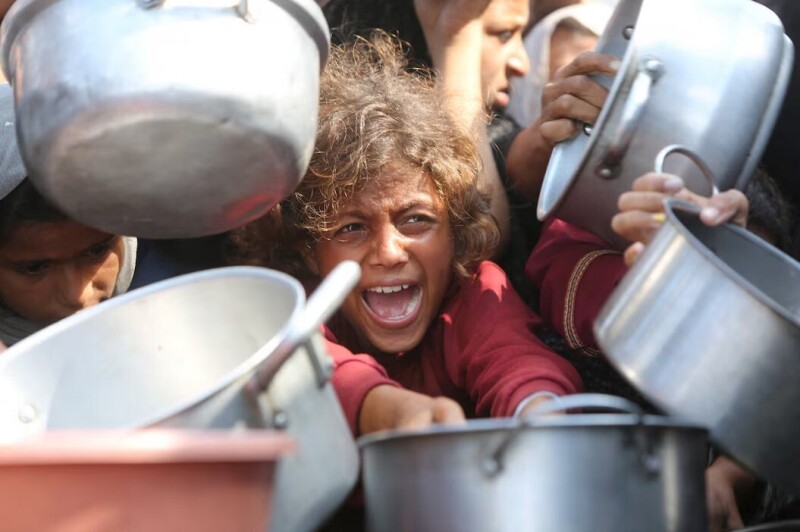 A child reacts surrounded by pots as Palestinians wait to receive food from a charity kitchen in Khan Younis, southern Gaza Strip, August 21, 2025. REUTERS