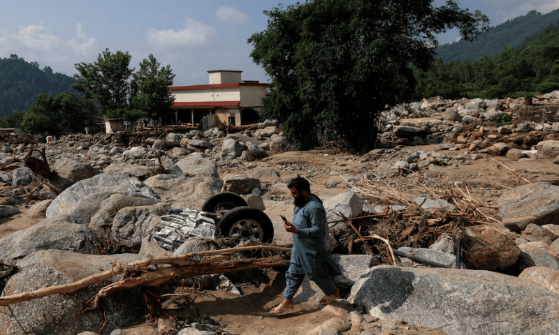A resident walks past the remains of a vehicle stucked amid rocks and boulders, following a storm that caused heavy rains and flooding in Qadir Nagar area, in Buner district, on August 21 2025. Reuters