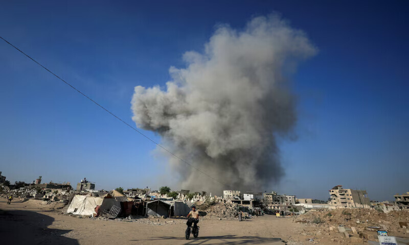 A Palestinian man rides a bike as smoke rises following an Israeli strike in Gaza City on Sunday. – Reuters
