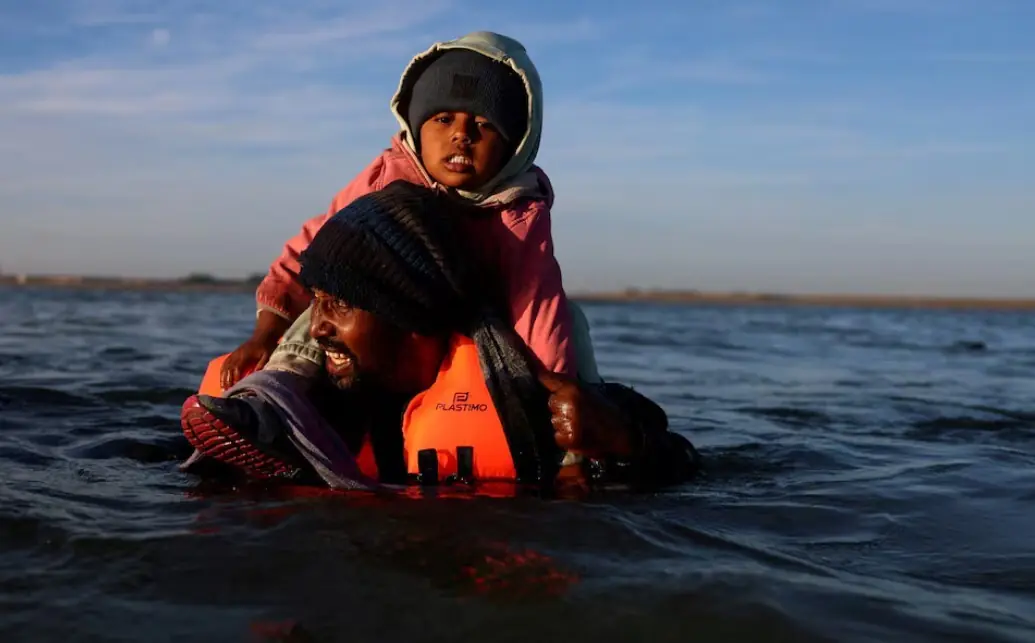 A migrant carrying a child wades through the sea in an attempt to board an inflatable dinghy leaving the coast of northern France to cross the English Channel to reach Britain, from the beach of Petit-Fort-Philippe in Gravelines, near Calais, France, August 25, 2025. REUTERS