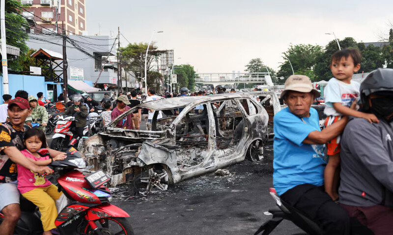 People travel past a car burnt during a protest over lawmakers’ pay outside East Jakarta’s police headquarters in Indonesia. – Reuters