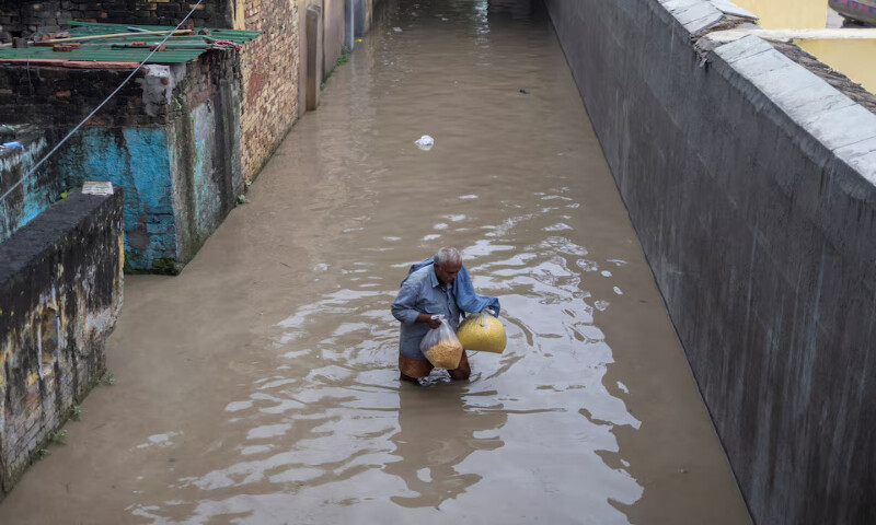 A man carries his belongings as he walks through a flooded alley in New Delhi, India. – Reuters