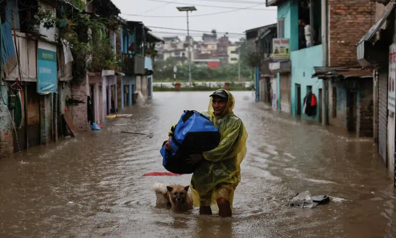 A man carries a bag as he wades through a flooded street along the bank of the overflowing Bagmati River following heavy rains in Kathmandu, Nepal. – Reuters