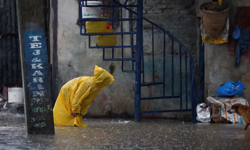 A woman wearing a raincoat wades through a flooded street along the bank of the overflowing Bagmati River following heavy rains in Kathmandu, Nepal. – Reuters