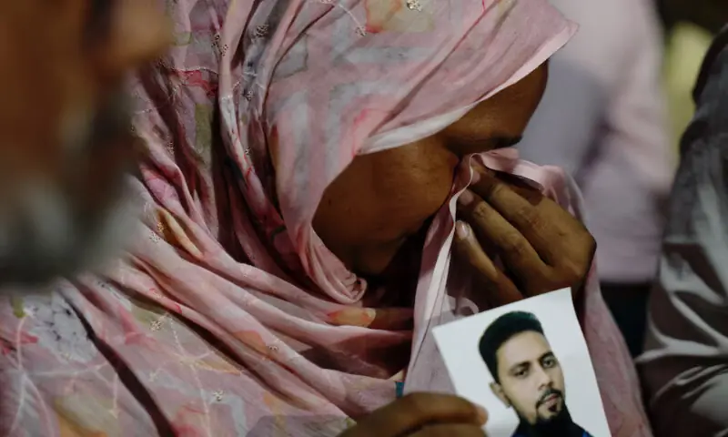 A relative mourns while holding a picture of a missing person following a fire that broke out at a garment factory and a chemical warehouse in Dhaka, Bangladesh, on Tuesday. – Reuters