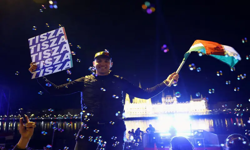 A man waves a flag and holds a poster as people celebrate following partial results on the day of the Hungarian Parliamentary election in Budapest, Hungary, on Monday. – Reuters