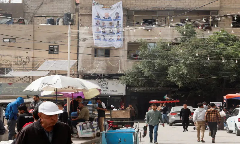 Palestinians walk past an electoral candidates list displayed in Deir Al Balah, central Gaza Strip. &ndash; Reuters