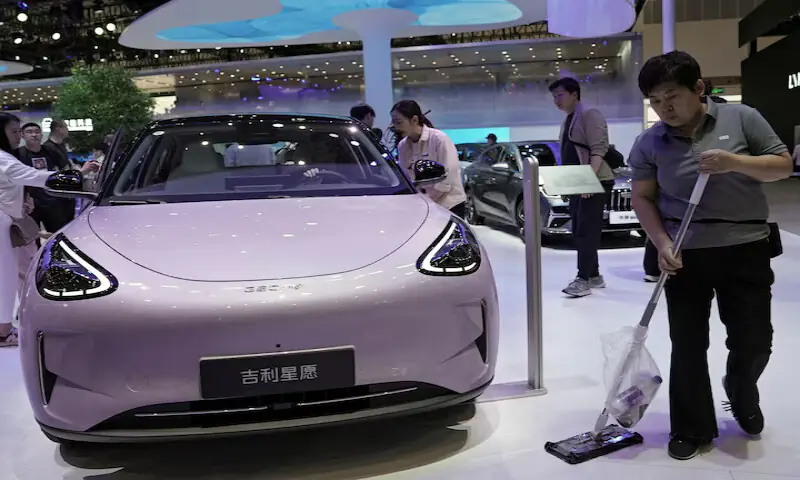 A staff member cleans the floor next to a Geely GEOME Xingyuan electric vehicle, also known as Geely EX2, displayed at the Beijing auto show. &ndash; Reuters