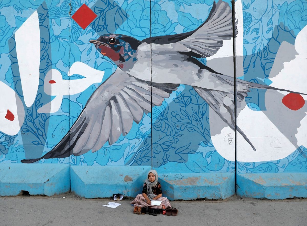 A shoe polishing girl waits for customers under graffiti on a wall in Kabul. Reuters