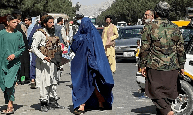 A woman walks past men from the Afghan Taliban. PHOTO: Al Arabiya