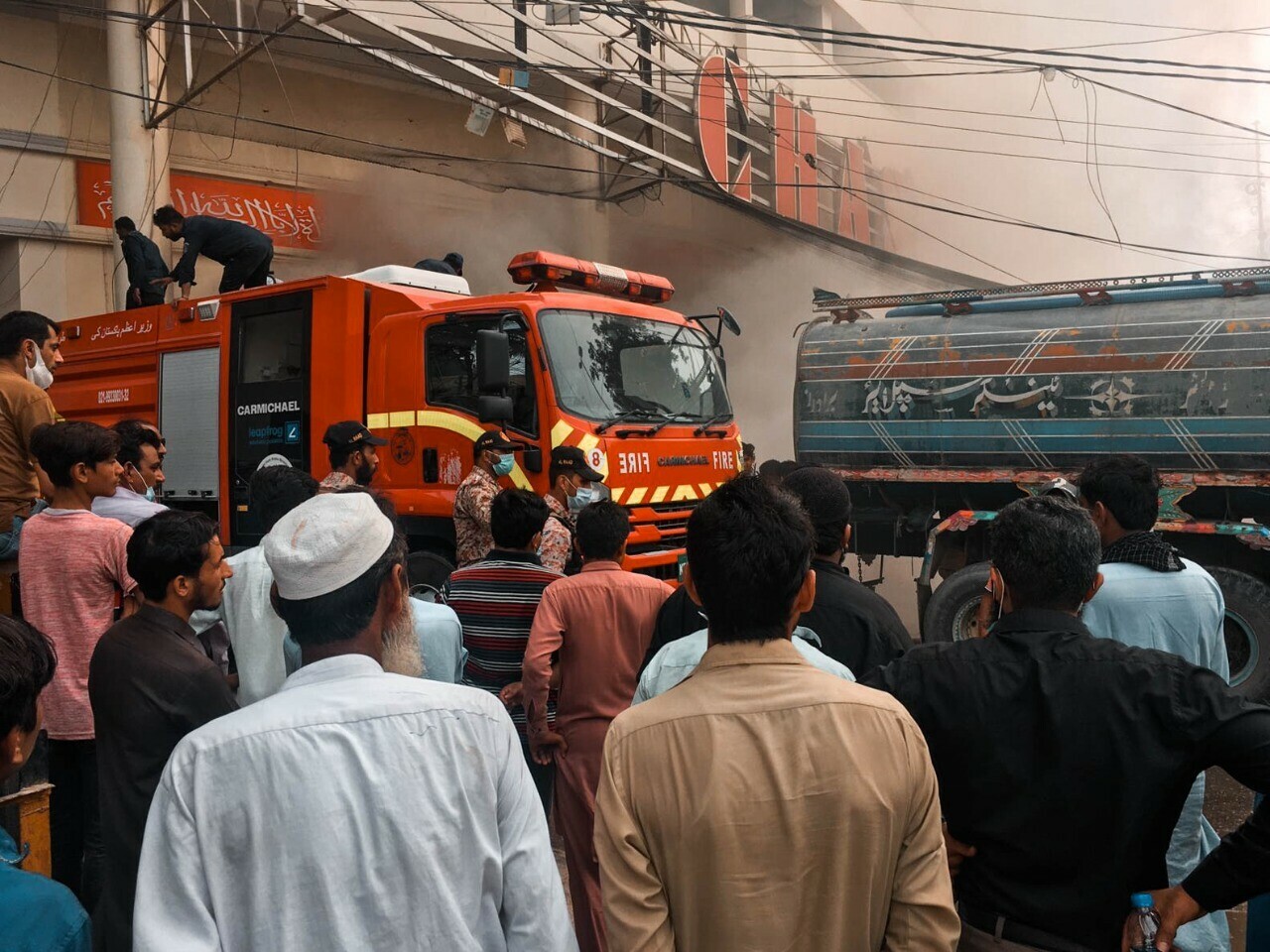 People stand outside the Chase departmental store in Karachi as the fire that started in the basement is yet to be brought under control. Photo: Haris Khan