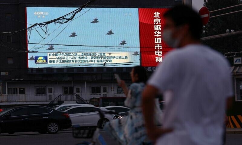 Pedestrians wait at an intersection near a screen showing footage of Chinese People’s Liberation Army (PLA) aircraft. Photo: Reuters.