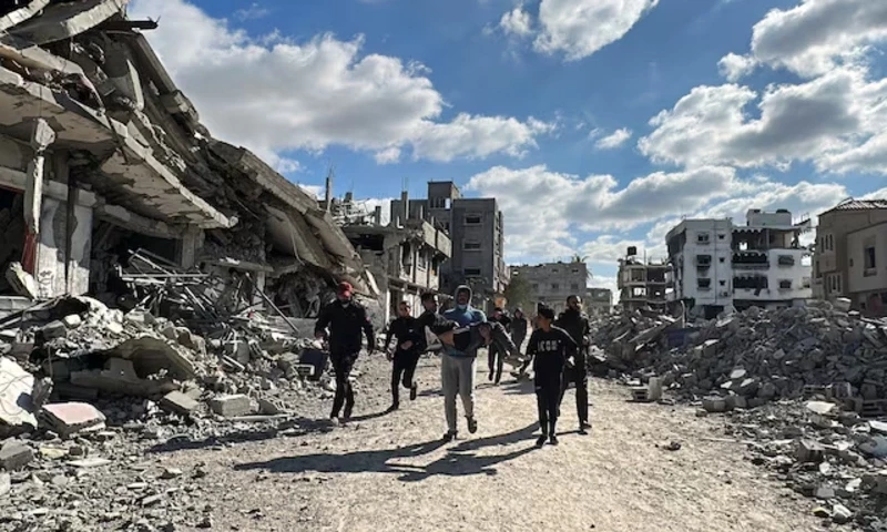 A man carries a wounded Palestinian as people walk past the rubble of houses and buildings destroyed during the war, following a ceasefire between Israel and Hamas, in Al-Bureij in the central Gaza Strip January 20, 2025. REUTERS