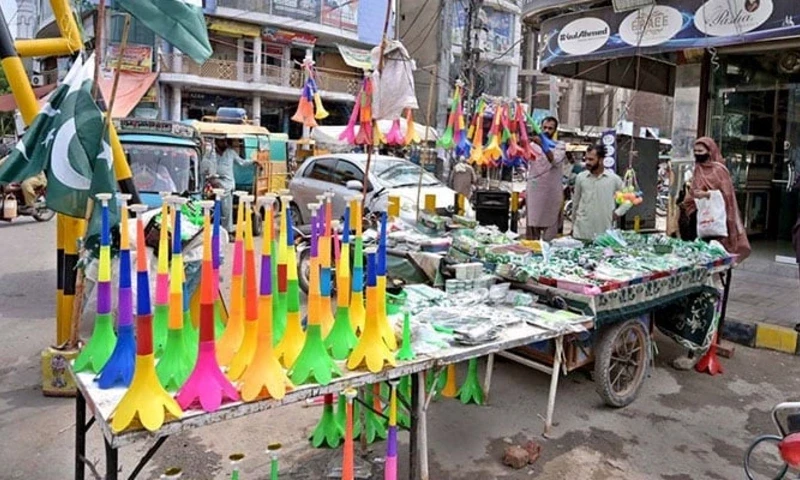Vendor displaying national flag badges and other festive items to attract customers ahead of the upcoming Independence Day celebrations at catchahry Bzaar, Sargodha. — APP Vendor displaying national flag badges and other festive items to attract customers ahead of the upcoming Independence Day celebrations at catchahry Bzaar, Sargodha. — APP