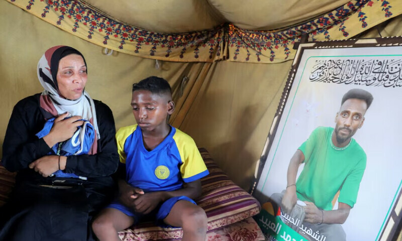 Doaa, the widow of late soccer player Suleiman Al-Obeid, known as the “Palestinian Pele,” who was killed by an Israeli strike targeting people waiting for humanitarian aid, according to the Palestine Football Association, looks at his picture while holding his shorts, as her son sits beside her inside their tent in Gaza City August 9, 2025. REUTERS Doaa, the widow of late soccer player Suleiman Al-Obeid, known as the “Palestinian Pele,” who was killed by an Israeli strike targeting people waiting for humanitarian aid, according to the Palestine Football Association, looks at his picture while holding his shorts, as her son sits beside her inside their tent in Gaza City August 9, 2025. REUTERS
