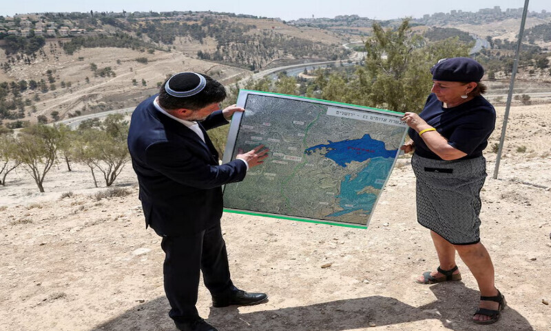 Israeli Finance Minister Bezalel Smotrich and a woman hold a map that shows the long-frozen E1 settlement scheme, that would split East Jerusalem from the occupied West Bank, on the day of a press conference near the Israeli settlement of Maale Adumim, in the Israeli-occupied West Bank, August 14, 2025. REUTERS Israeli Finance Minister Bezalel Smotrich and a woman hold a map that shows the long-frozen E1 settlement scheme, that would split East Jerusalem from the occupied West Bank, on the day of a press conference near the Israeli settlement of Maale Adumim, in the Israeli-occupied West Bank, August 14, 2025. REUTERS