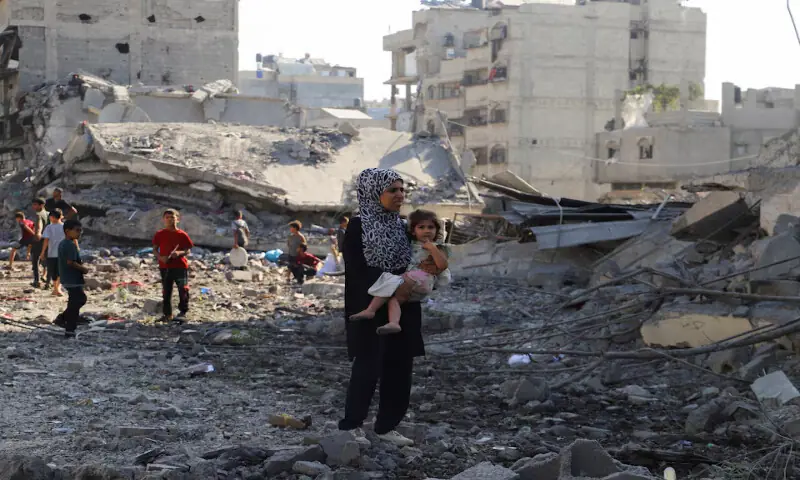 A Palestinian woman carries a child as she inspects the site of an Israeli strike on a house in Gaza City on Tuesday. – Reuters A Palestinian woman carries a child as she inspects the site of an Israeli strike on a house in Gaza City on Tuesday. – Reuters