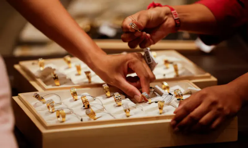 A salesperson shows a gold ring to customers at a jewellery showroom in Ahmedabad, India, October 8, 2025.//REUTERS A salesperson shows a gold ring to customers at a jewellery showroom in Ahmedabad, India, October 8, 2025.//REUTERS
