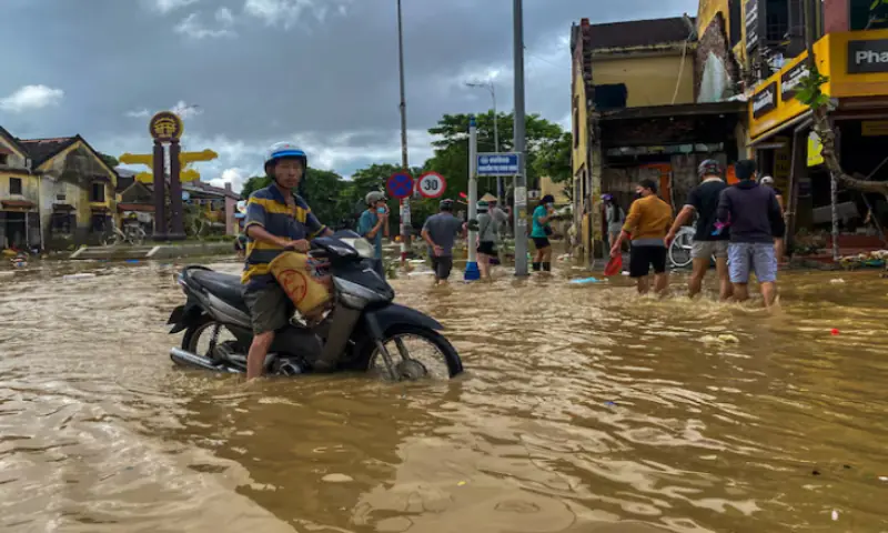 People wade through a flooded street, as a motorist looks on, in Hoi An, following deadly floods in central Vietnam, October 31, 2025//REUTERS