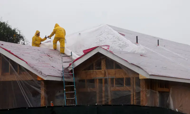 Workers stand on a roof as heavy rains fall in Altadena, California. &ndash; Reuters