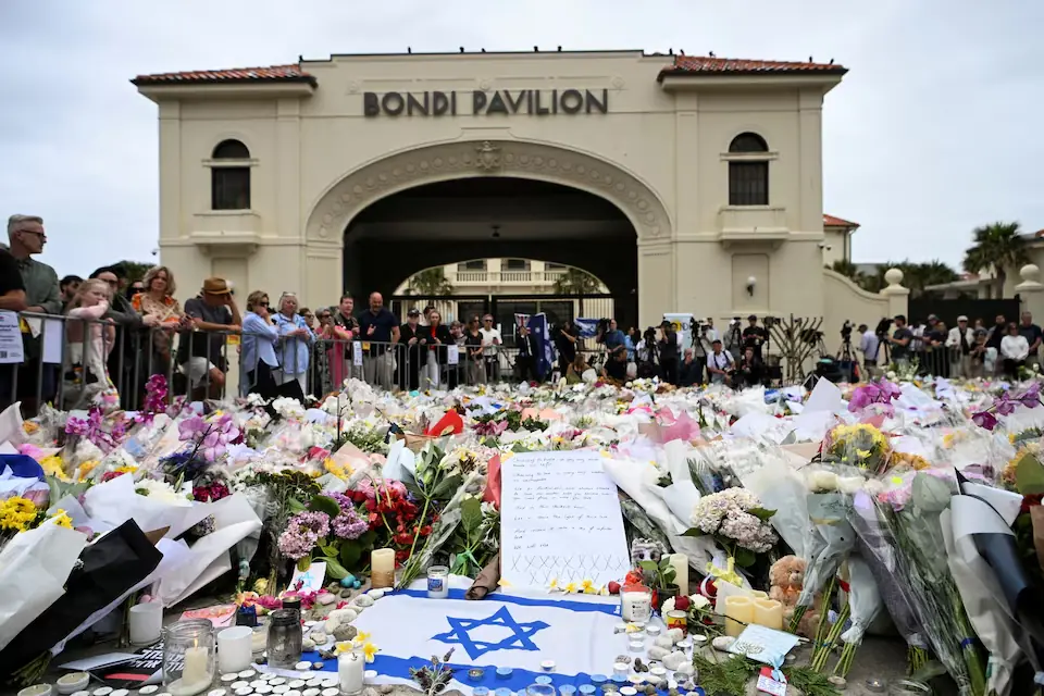 People stand near flowers laid as a tribute at Bondi Beach to honour the victims of a mass shooting that targeted a Hanukkah celebration at Bondi Beach. &ndash; Reuters