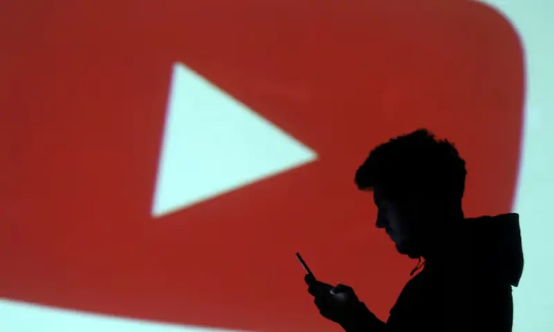A silhouette of a mobile user is seen next to a screen projection of the YouTube logo in this picture illustration taken. &ndash; Reuters
