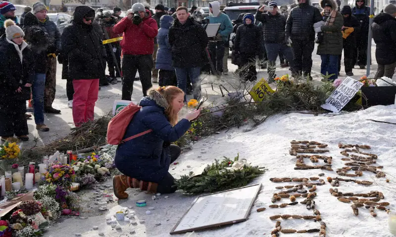A woman clears snow from a picture of Alex Pretti at a makeshift memorial in Minneapolis, Minnesota, US. &ndash; Reuters