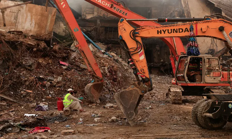 A worker takes a break next to heavy machinery used to clear the site following a massive fire in the Gul Plaza Shopping Mall in Karachi. &ndash; Reuters