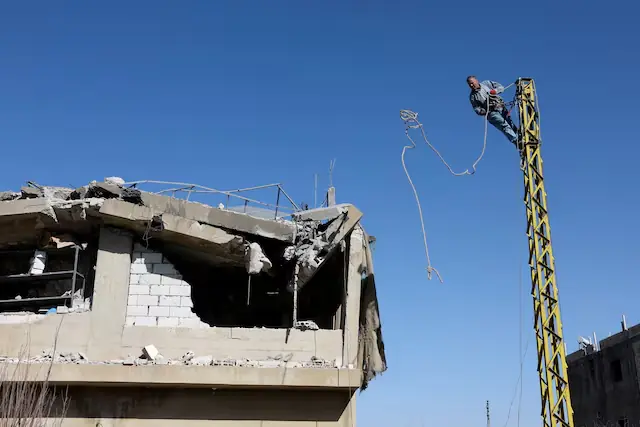 A man works on an electric pole next to a damaged building, in the aftermath of an Israeli strike on Friday, in Tamnine el Tahta, Bekaa Valley, Lebanon. &ndash; Reuters