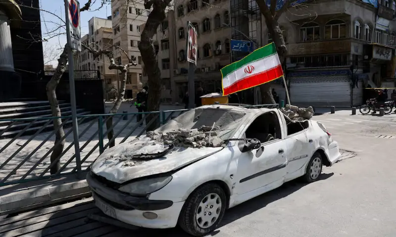 An Iranian flag mounted on a damaged car following an air strike on a police station in Tehran. &ndash; Reuters