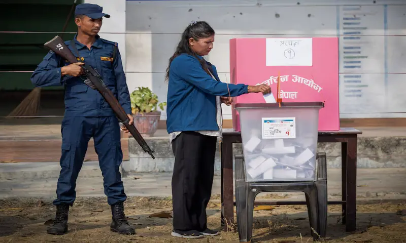 A woman casts her vote as a security officer stands guard at a polling station at a village, in Jhapa district, Nepal. &ndash; Reuters