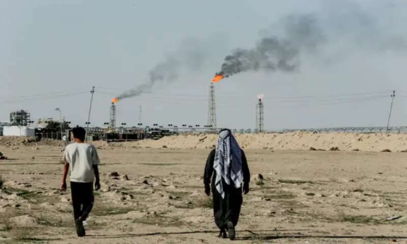 People walk near farmland by the Zubair oil field as gas flares rise in the distance, in Zubair Mishrif, Basra, Iraq, amid regional tensions following the recent disruption to shipping in the Strait of Hormuz and the US-Israeli conflict with Iran. &ndash; Reuters