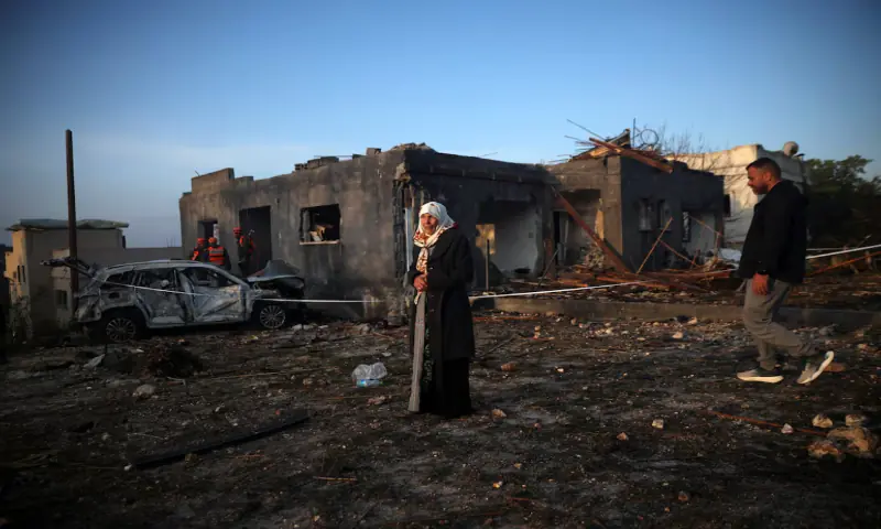 A woman stands as Israeli emergency responders work at the site of an impact by an Iranian missile, amid the US-Israel conflict with Iran, in northern Israel. &ndash; Reuters