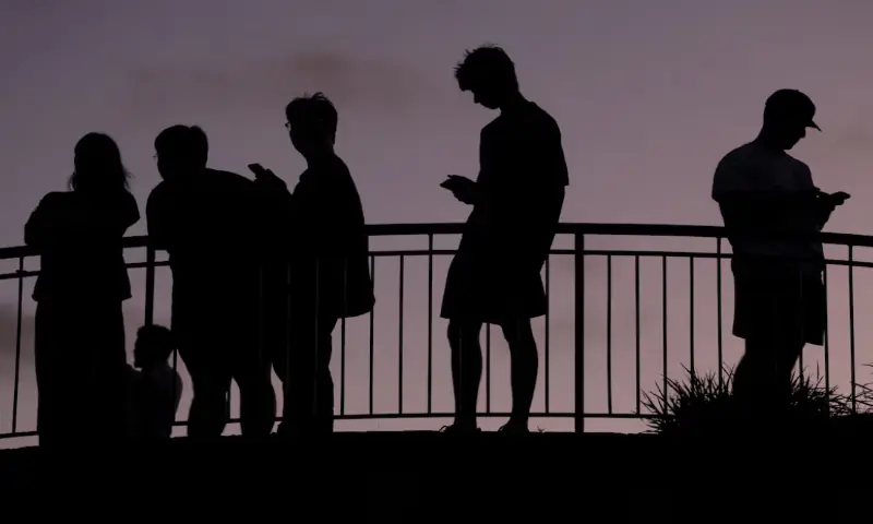 People use their mobile phones at dusk in Brisbane, Australia. &ndash; Reuters