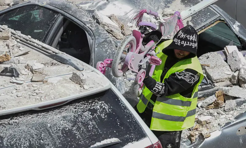 A man wearing a high-visibility vest carries a child&rsquo;s bicycle at an impact site following a barrage of missiles launched from Iran in central Israel. &ndash; Reuters