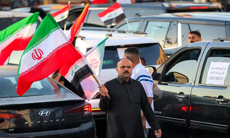 A man holds an Iranian flag as he moves between vehicles during celebrations welcoming the two-week ceasefire between the United States and Iran in Baghdad&rsquo;s central Tahrir Square on April 8, 2026. AFP