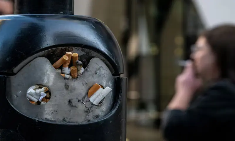 A smoker stands next to a bin for cigarette butts in London, Britain. &ndash; Reuters