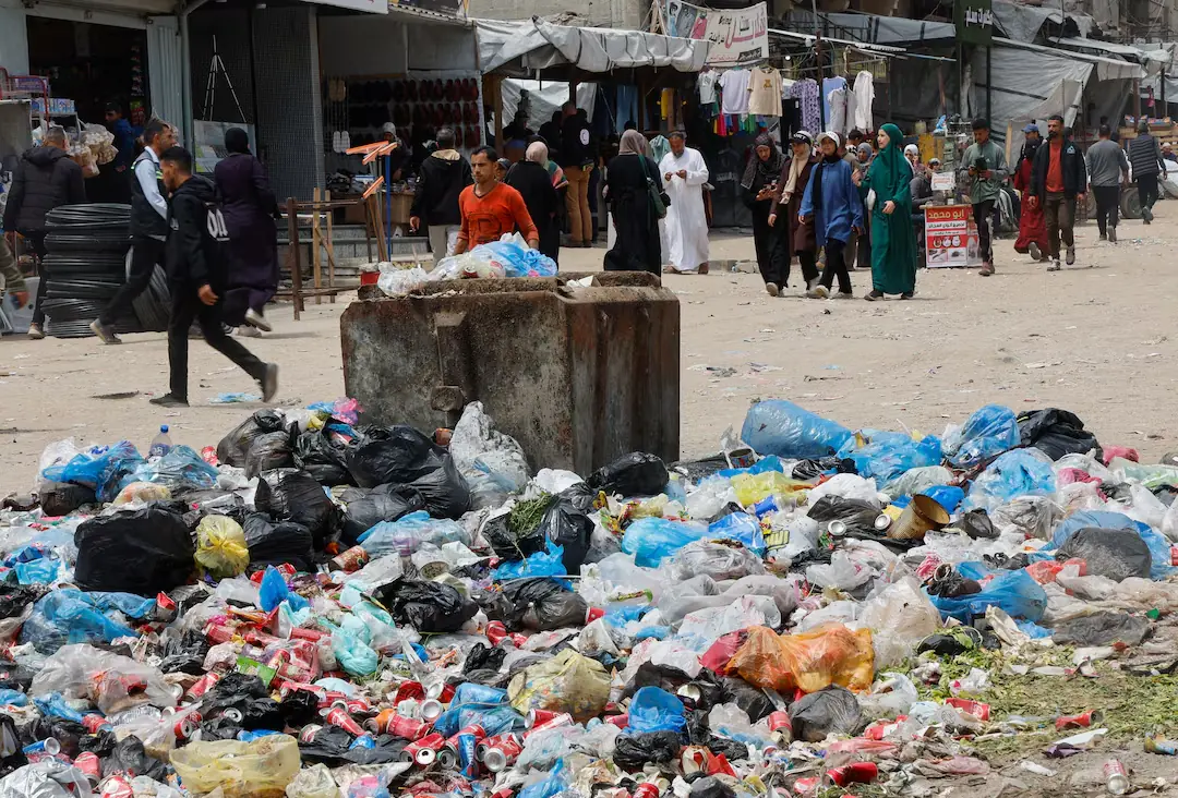 Palestinians walk past piles of garbage and waste near tents for displaced people, amid the spread of rodents, in Khan Younis in the southern Gaza Strip. -- Reuters
