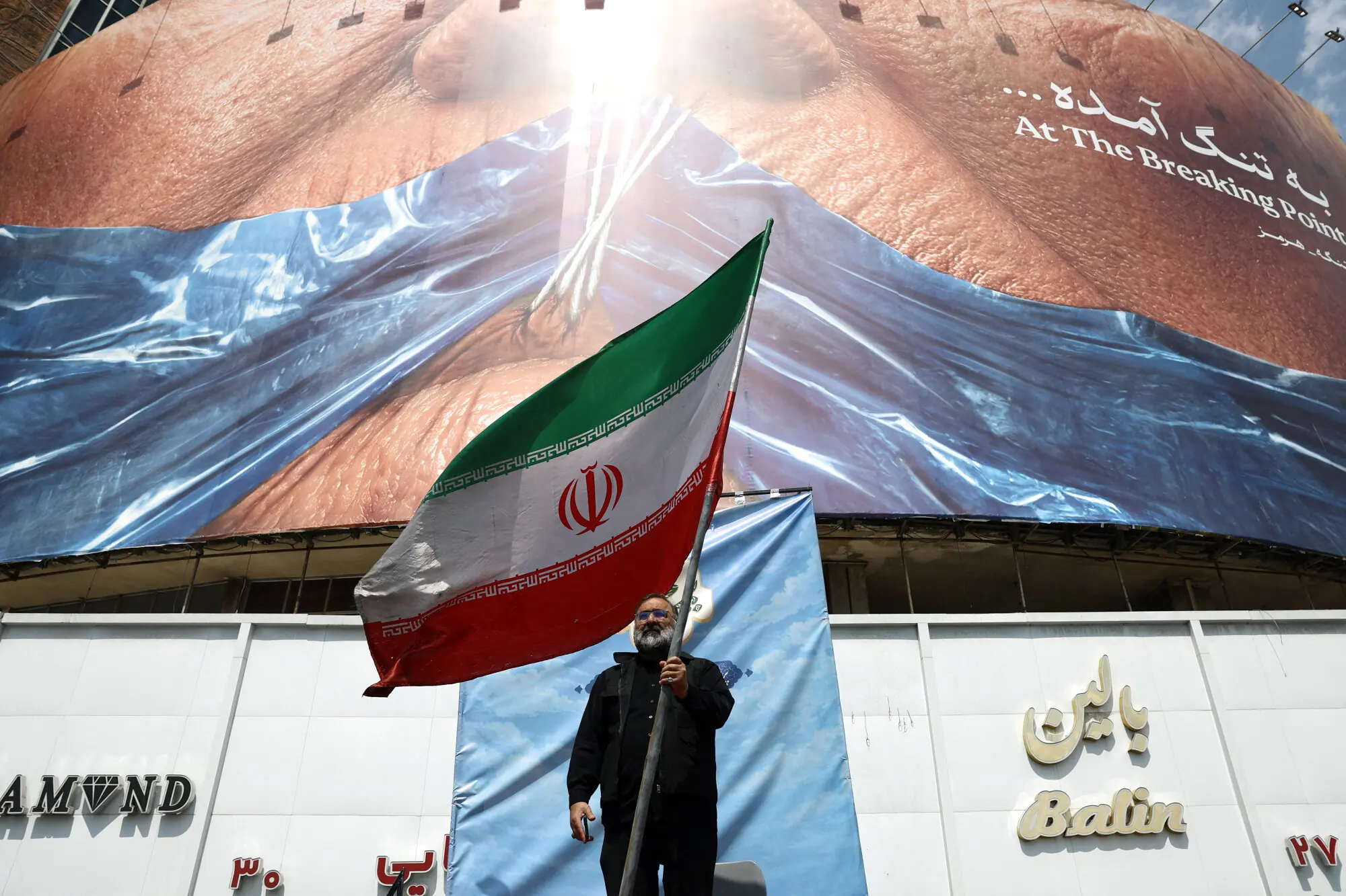 A man holds an Iranian flag near an anti-US billboard depicting US President Donald Trump and the Strait of Hormuz, in Tehran, Iran. -- Reuters