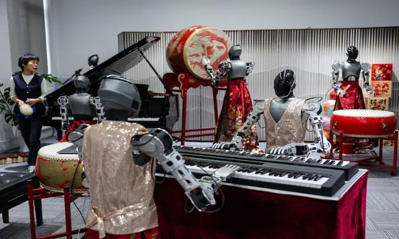 An ensemble of humanoid robots produced by Linkerbot is set up with musical instruments as a woman holding a wipe walks nearby, at the company&rsquo;s office in Beijing, China. -- Reuters