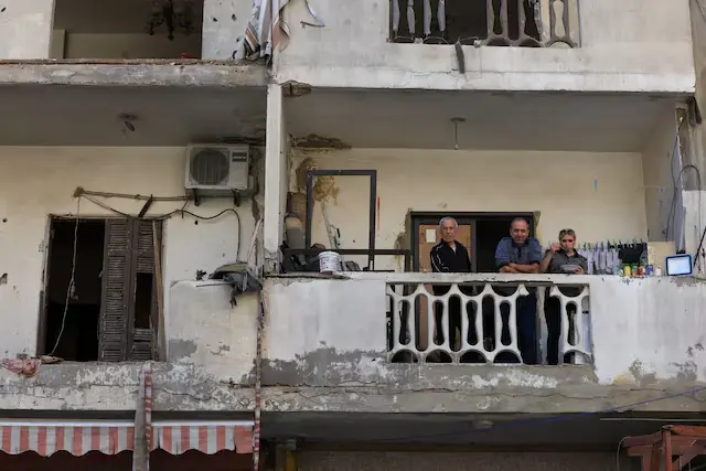 People sit in a balcony near the site of an Israeli strike that took place before a temporary ceasefire went into effect, in the southern suburbs of Beirut, Lebanon. --Reuters
