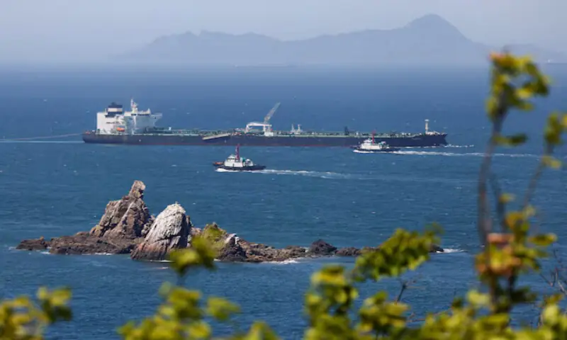 Tugboats guide a crude oil tanker passing through the Strait of Hormuz. -- Reuters