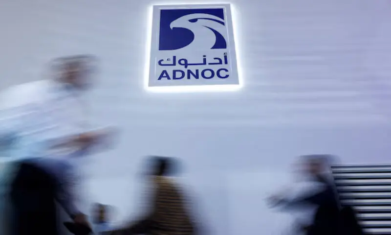 People walk past a logo of Abu Dhabi National Oil Company at a conference in Abu Dhabi, on November 3, 2025. Reuters